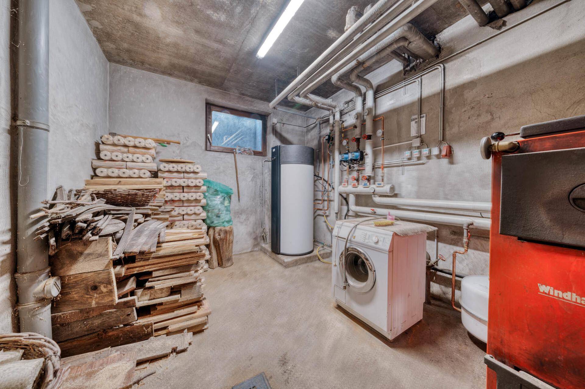 Heizungsraum mit Waschmaschine, Holzstapel und technischen Installationen.