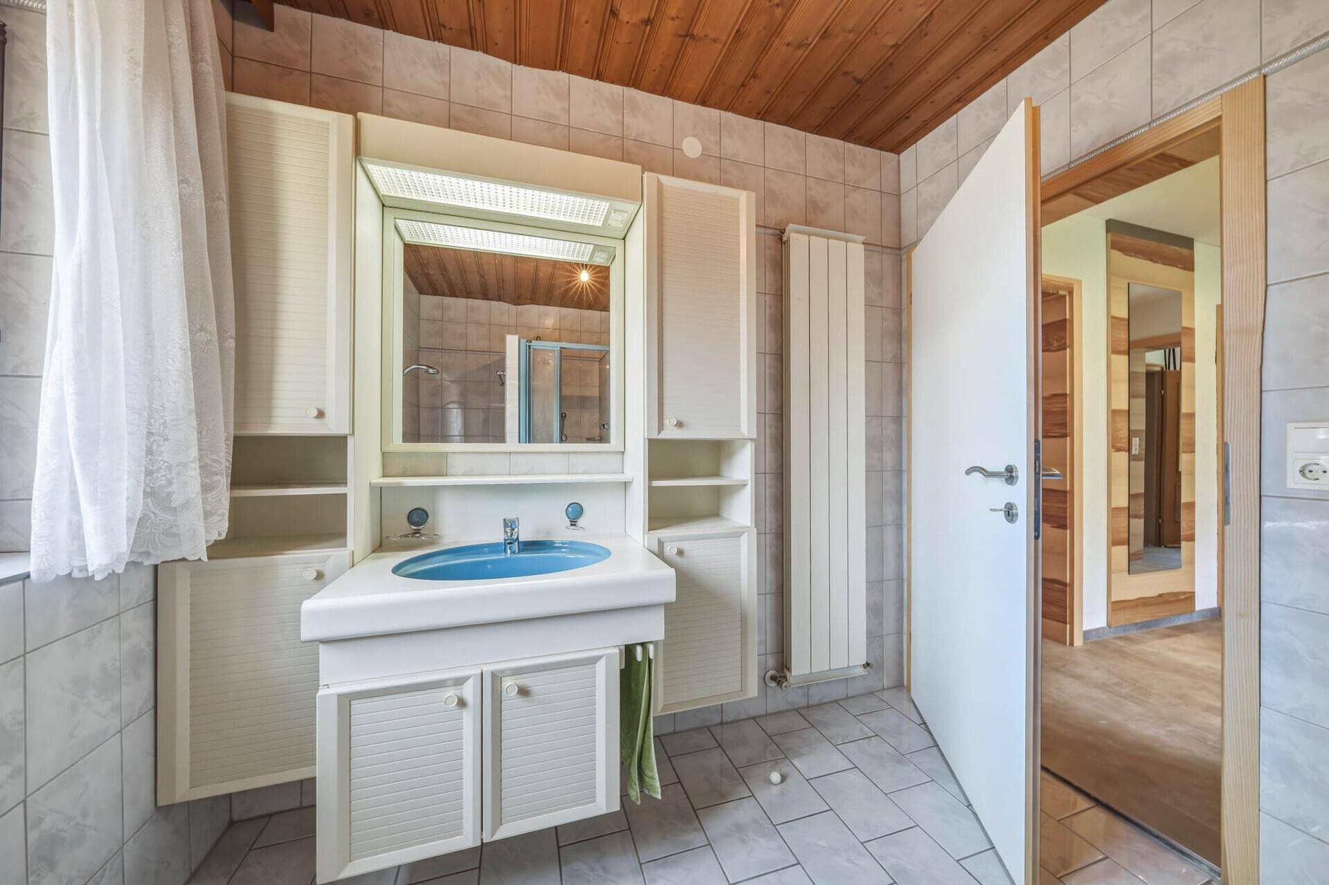 Badezimmer mit blauer Waschtischarmatur, Spiegelschrank und Holzdecke im traditionellen Stil.