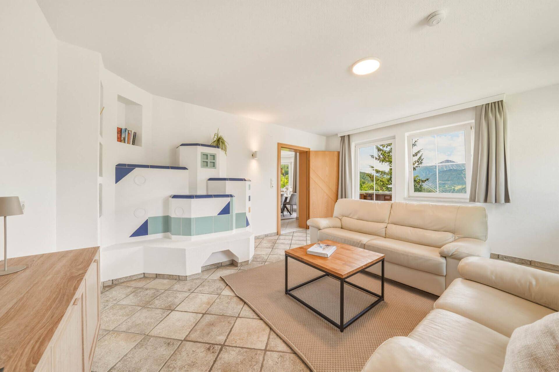 Gemütliches Wohnzimmer mit Kachelofen, bequemen Sofas und Bergblick.