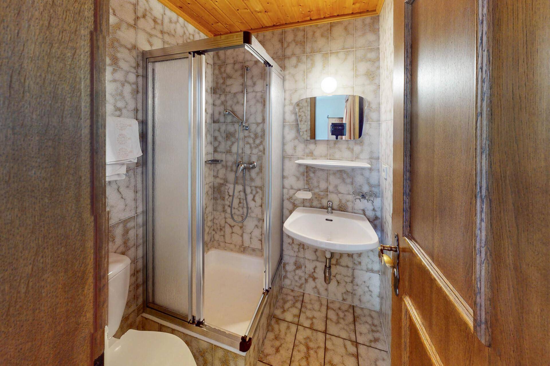 Kleines Badezimmer mit Duschkabine, WC, Waschbecken und Fliesen.