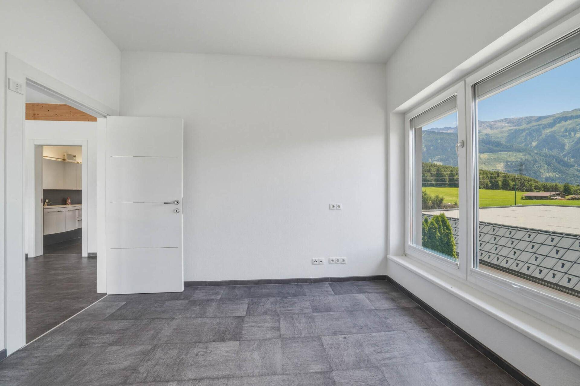 Helles Zimmer mit modernen Fliesen und Zugang zu einem weiteren Raum, ideal für flexible Nutzung.