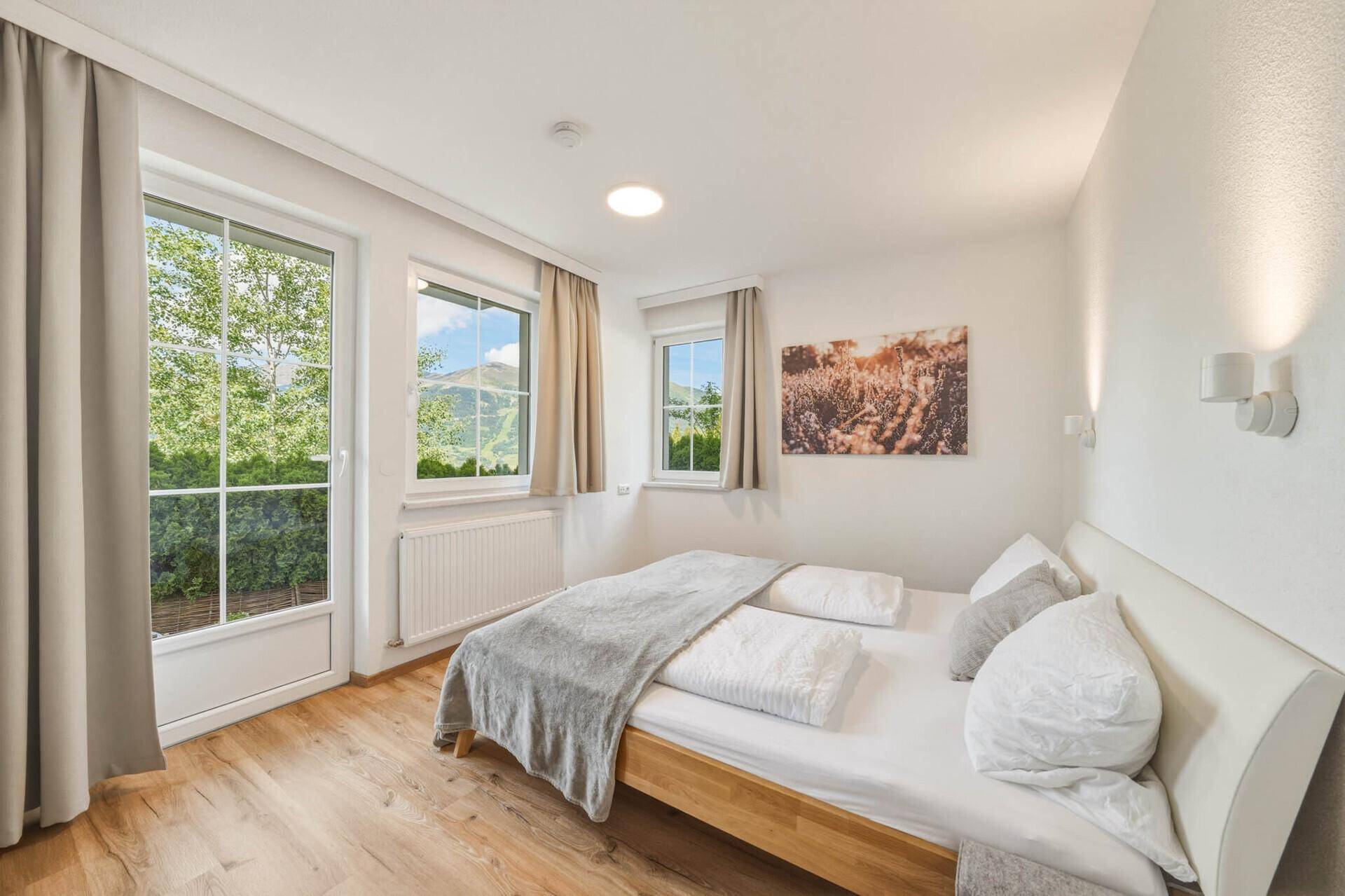 Helles Schlafzimmer mit Holzboden, Doppelbett und Zugang zu einem Außenbereich durch eine Fenstertür.