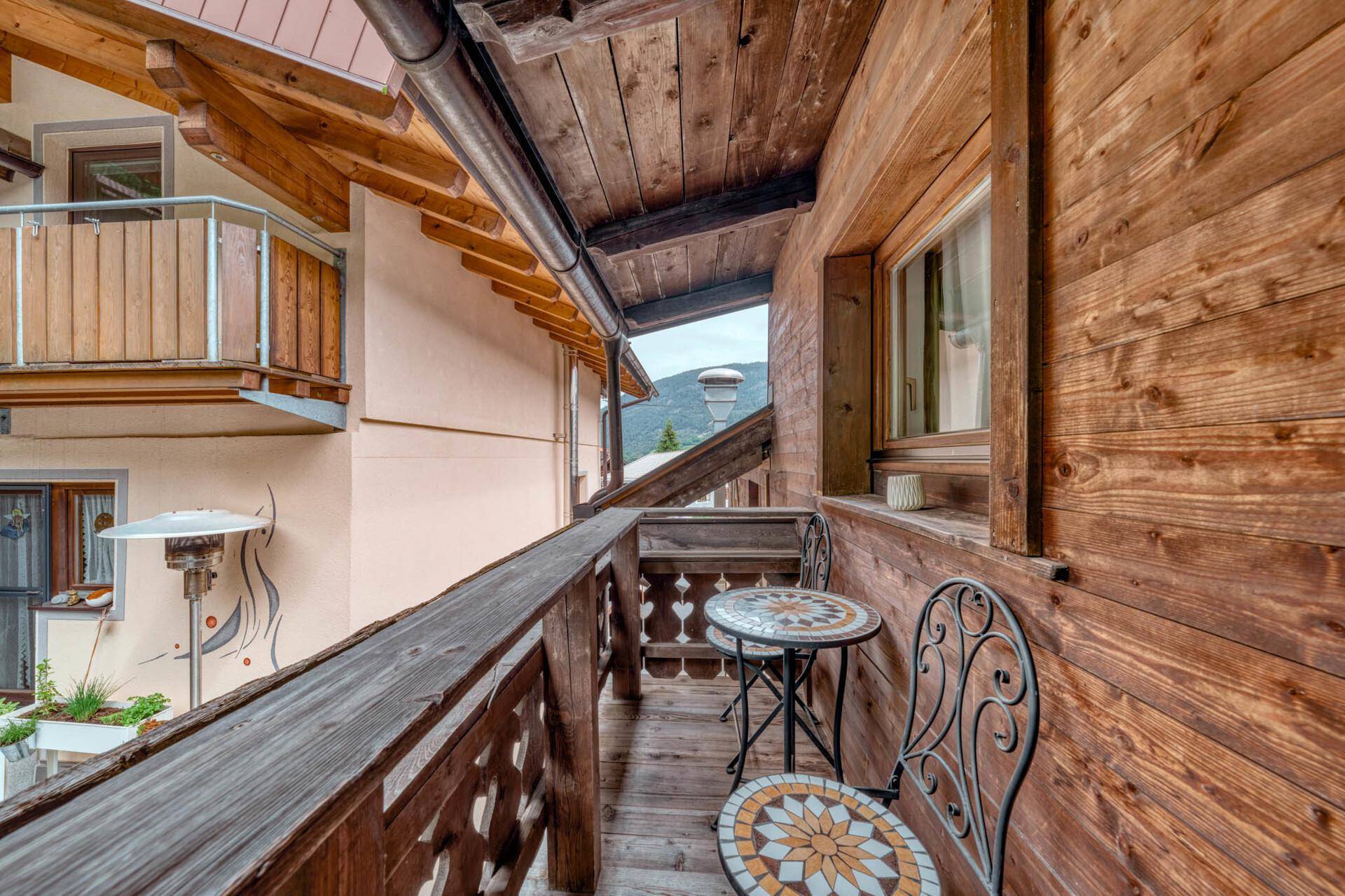 Traditioneller Holzbalkon mit schmiedeeisernen Möbeln und Blick auf die umliegende Berglandschaft.