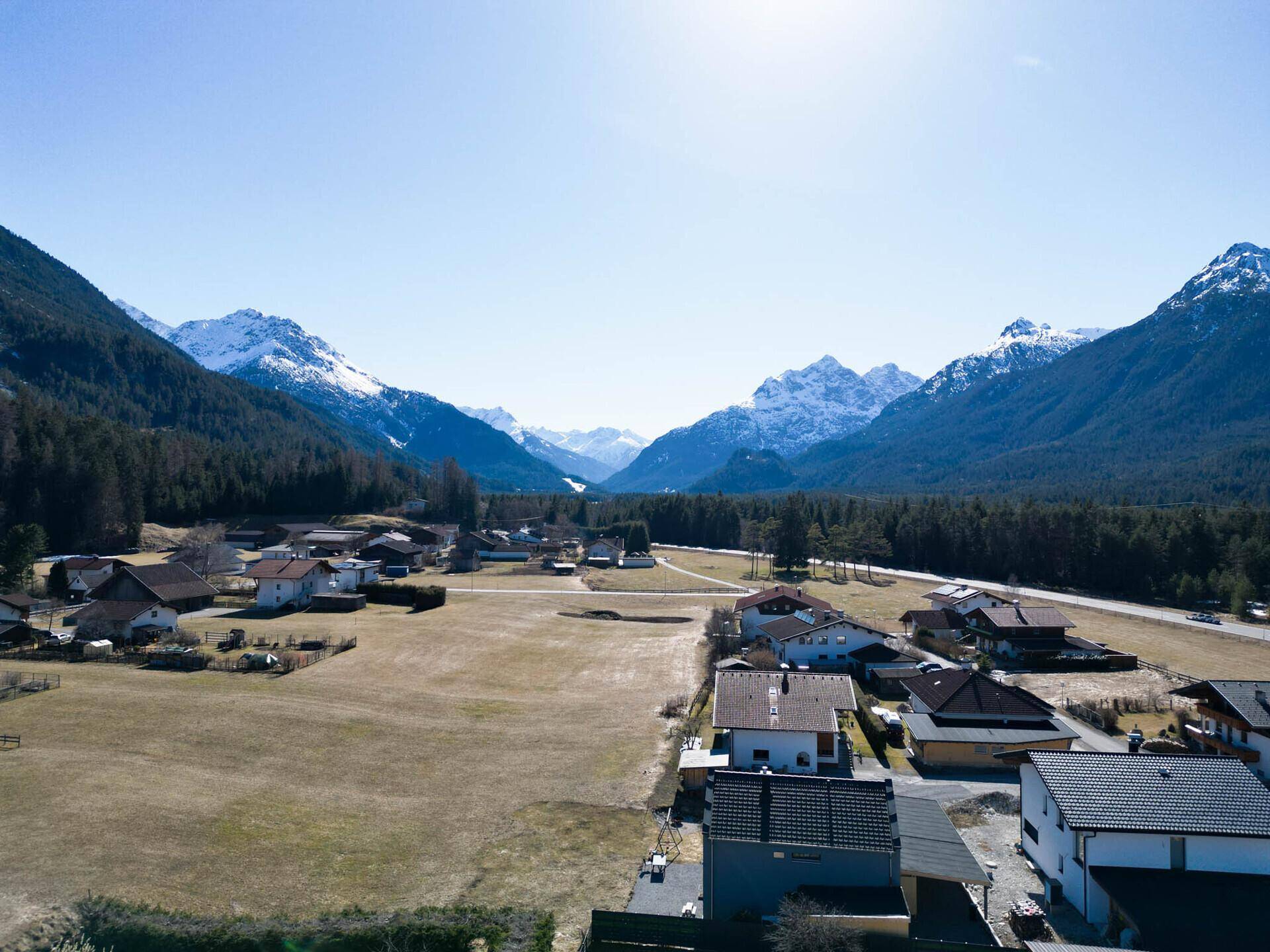Weitläufige Luftaufnahme eines Tals mit einem Dorf, Feldern und schneebedeckten Bergen in der Ferne.