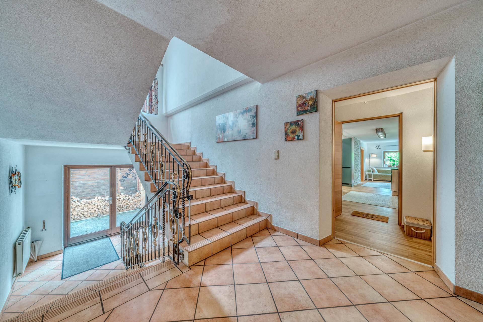 Heller Eingangsbereich mit gefliester Treppe, schmiedeeisernem Geländer und Holztür.