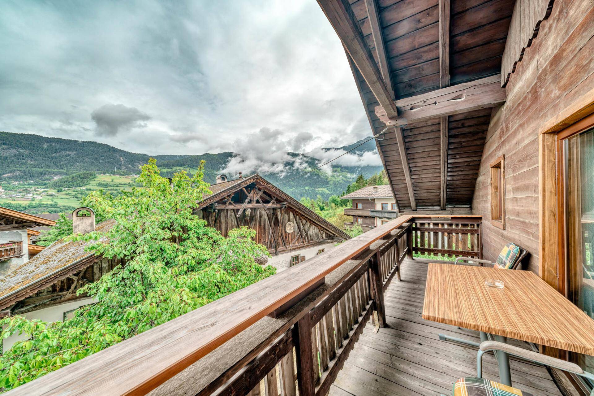 Geräumiger Holzbalkon mit Sitzgelegenheiten und weitem Blick auf die umliegende Berglandschaft.