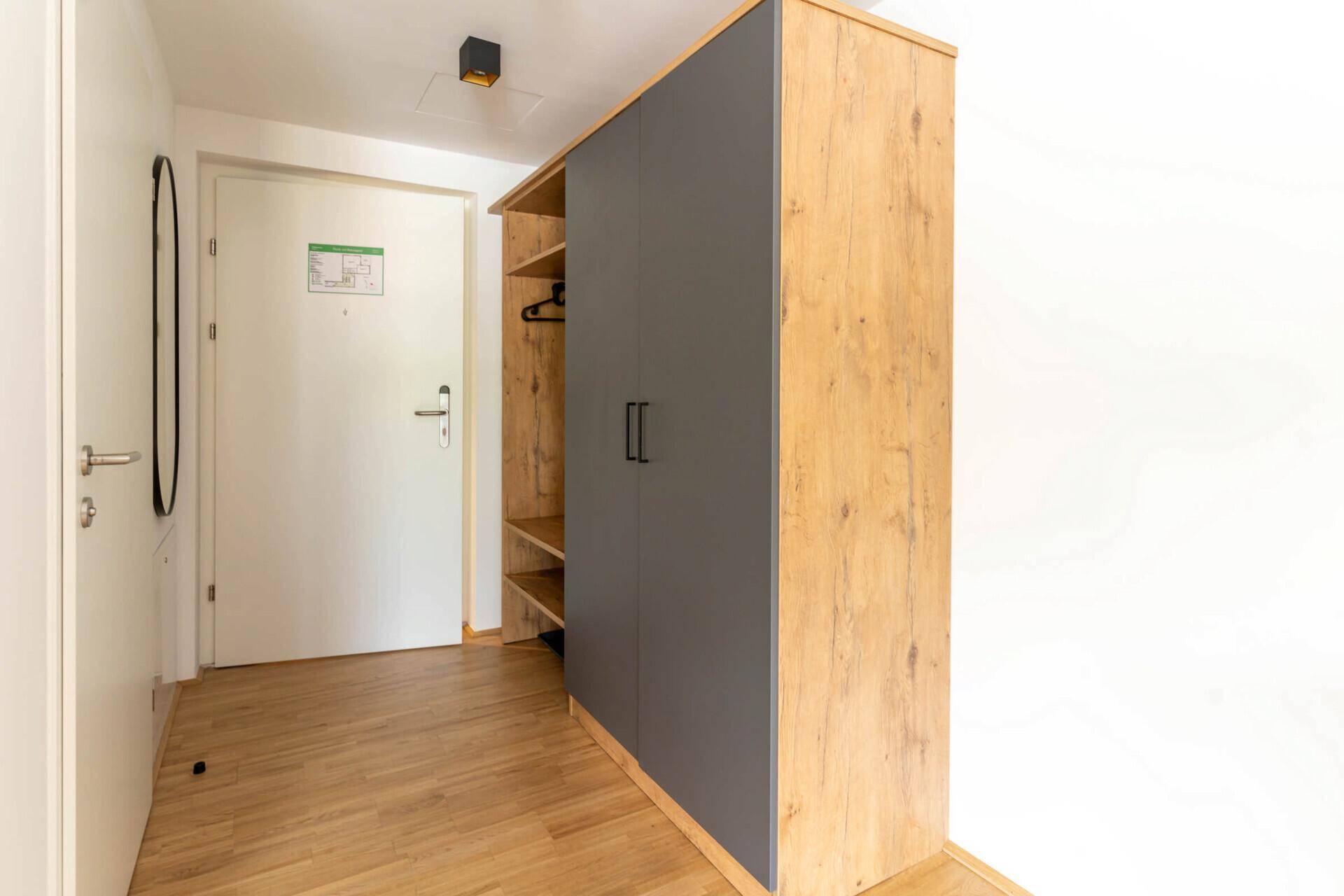Eingangsbereich mit Holzboden, Garderobenschrank und ovalem Wandspiegel.