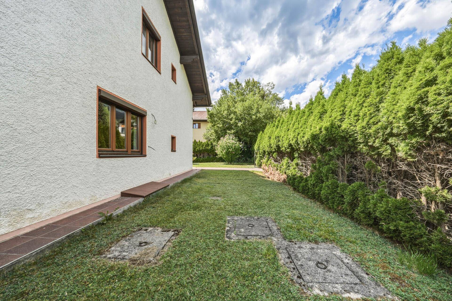 Seitenansicht des Hauses mit grüner Hecke und gepflegtem Rasenbereich.
