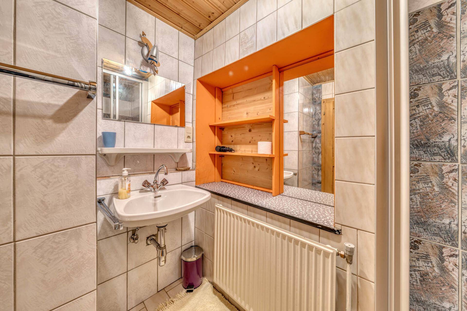 Badezimmer mit Waschbecken, Spiegel und Heizkörper, helle Fliesen und Holzdetails.