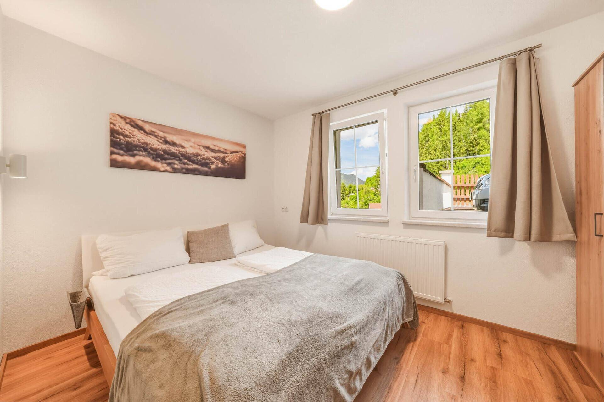 Helles Schlafzimmer mit Holzboden, Kleiderschrank und Blick ins Grüne.