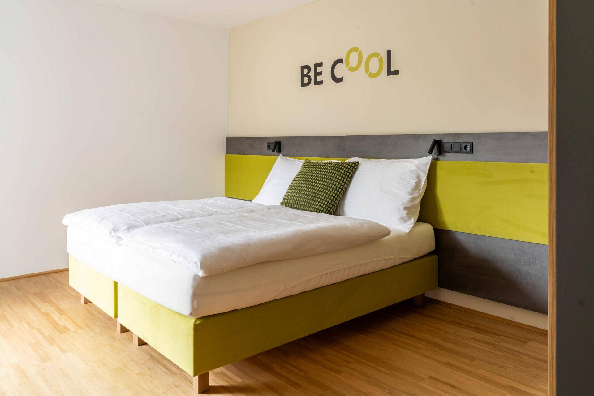 Helles Schlafzimmer mit Doppelbett, Holzboden und Fenster mit Vorhängen.