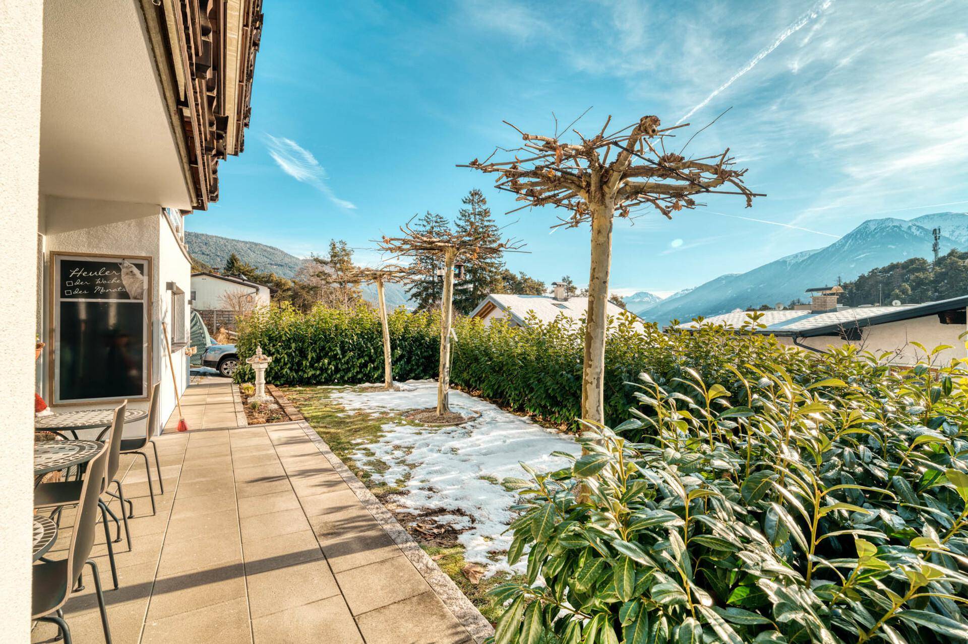 Gartenbereich mit Terrasse, Bäumen und Blick auf die Berge im Winter.
