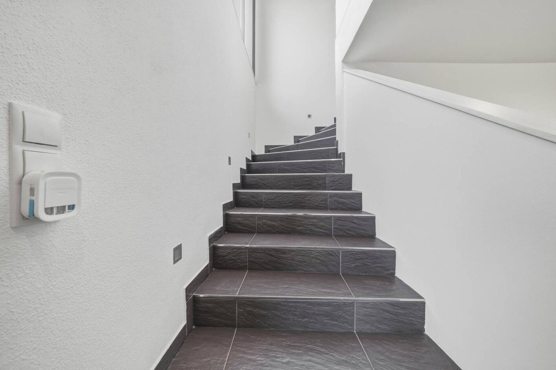 Elegante Treppe mit dunklen Fliesen und weiß gestrichenen Wänden, die in die obere Etage führt.