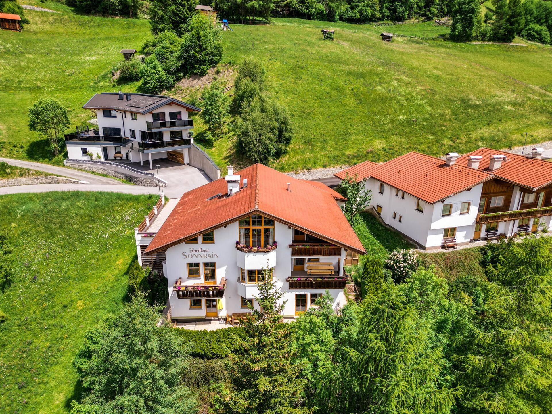 Luftaufnahme des Anwesens in einer grünen Berglandschaft, umgeben von weiteren Häusern.