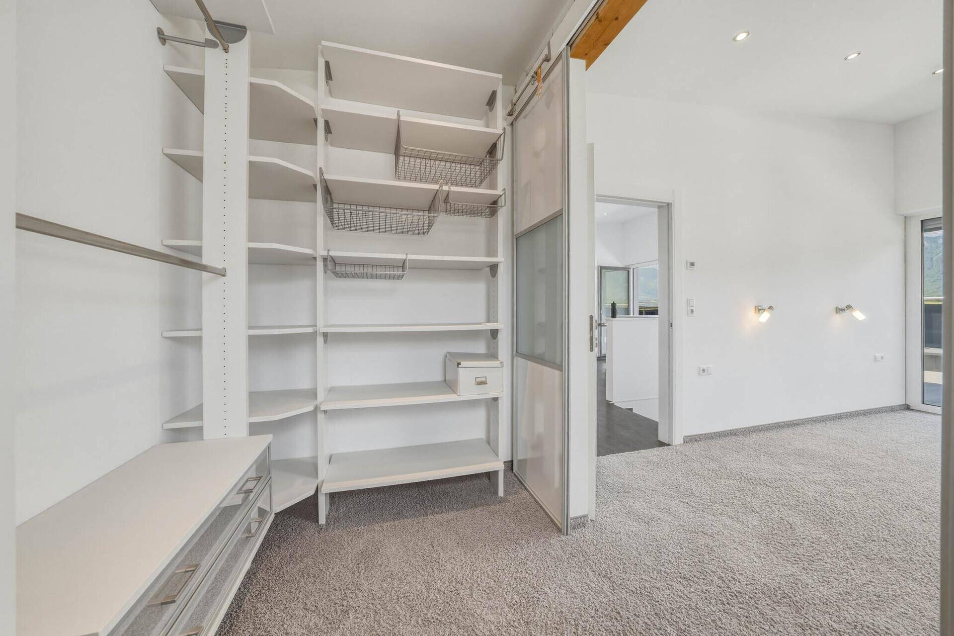Begehbarer Kleiderschrank mit integrierten Regalen und Stauraum, angrenzend an einen Wohnbereich.