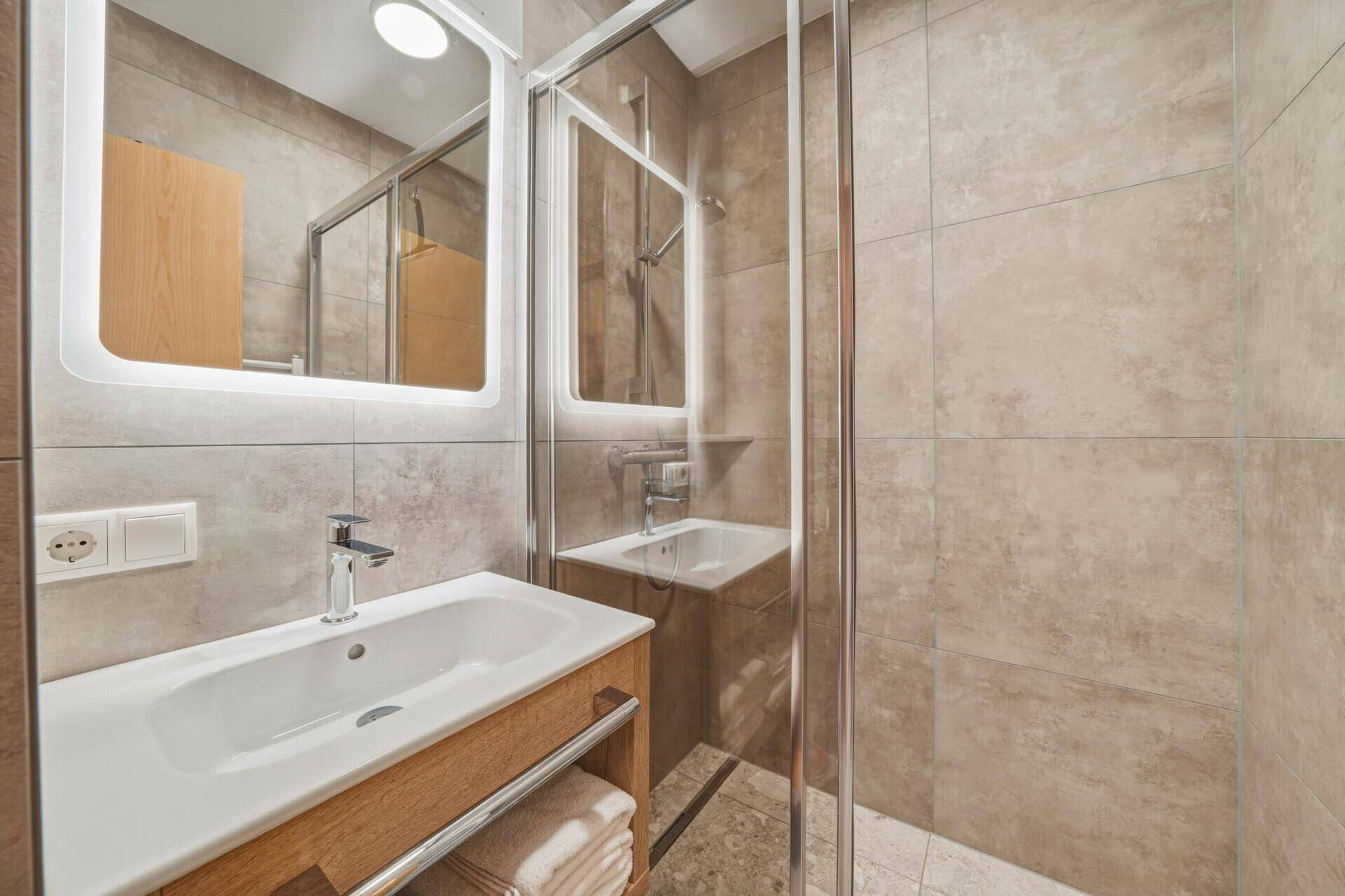 Modernes Badezimmer mit begehbarer Dusche, beleuchtetem Spiegel und eleganten Fliesen.