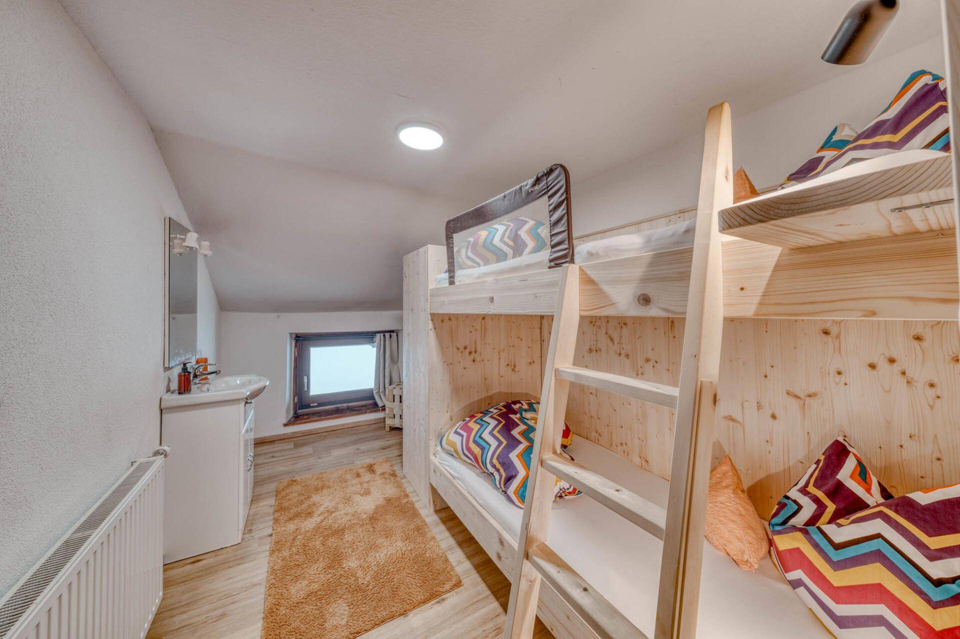 Helles Schlafzimmer mit Etagenbetten aus hellem Holz und einem kleinen Waschbecken.