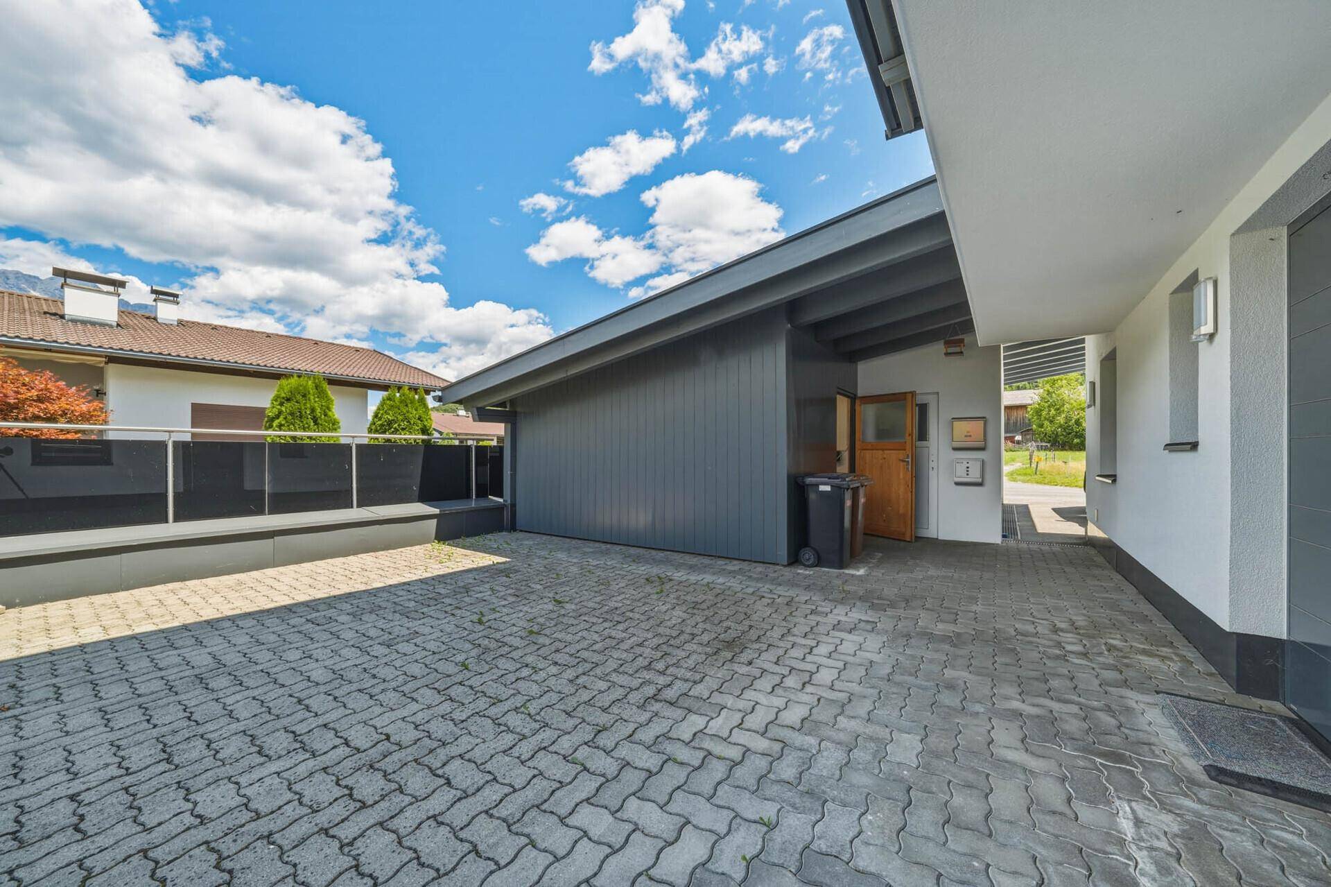 Gepflasterte Einfahrt führt zu einem überdachten Parkbereich oder Carport.