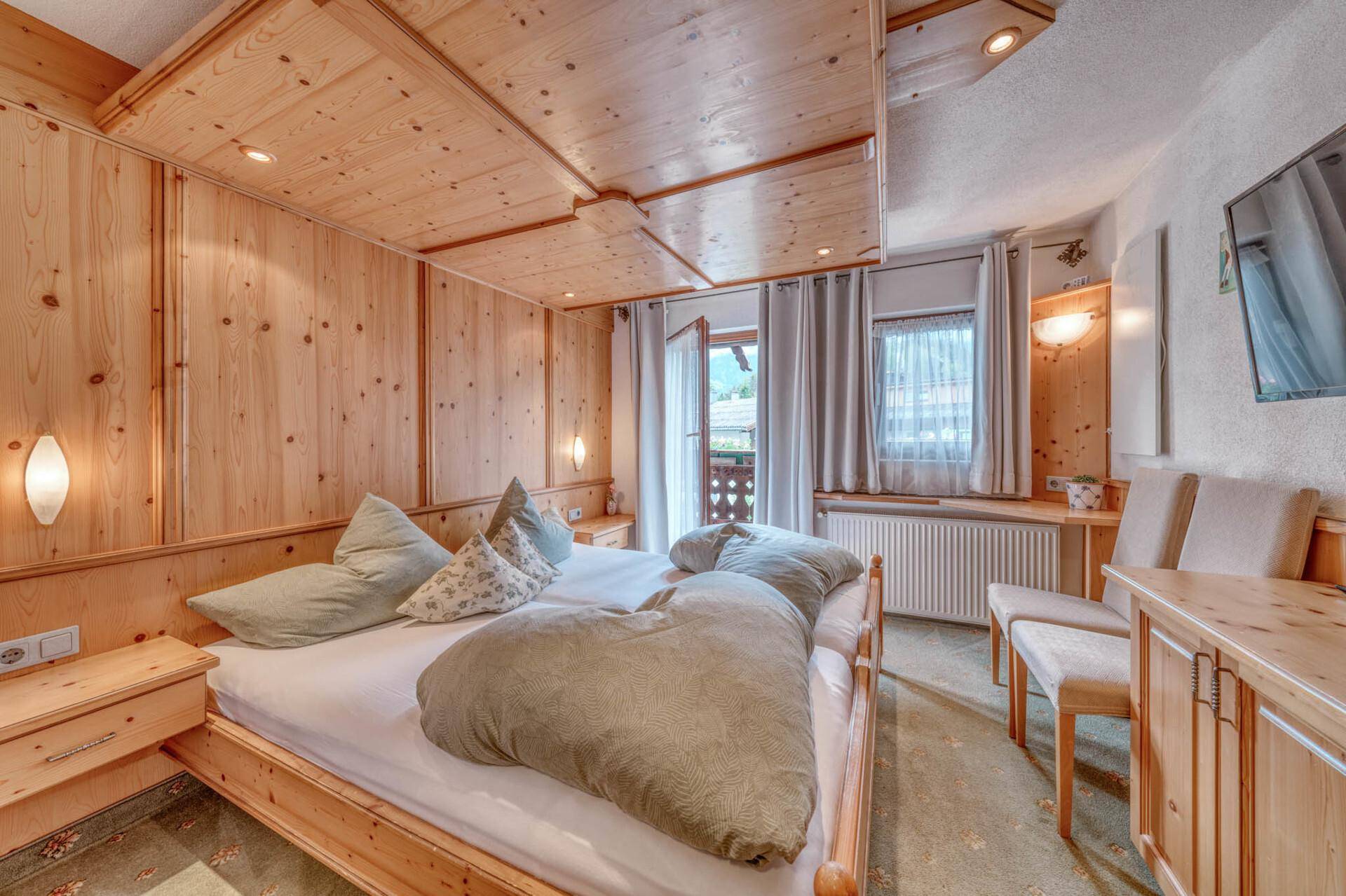 Rustikales Schlafzimmer mit viel Holzvertäfelung, Doppelbett und Zugang zum Balkon.