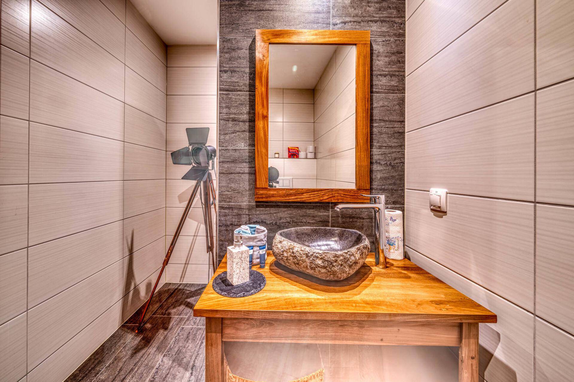 Modernes Gäste-WC mit Natursteinwaschbecken, Holzwaschtisch und großem Spiegel.