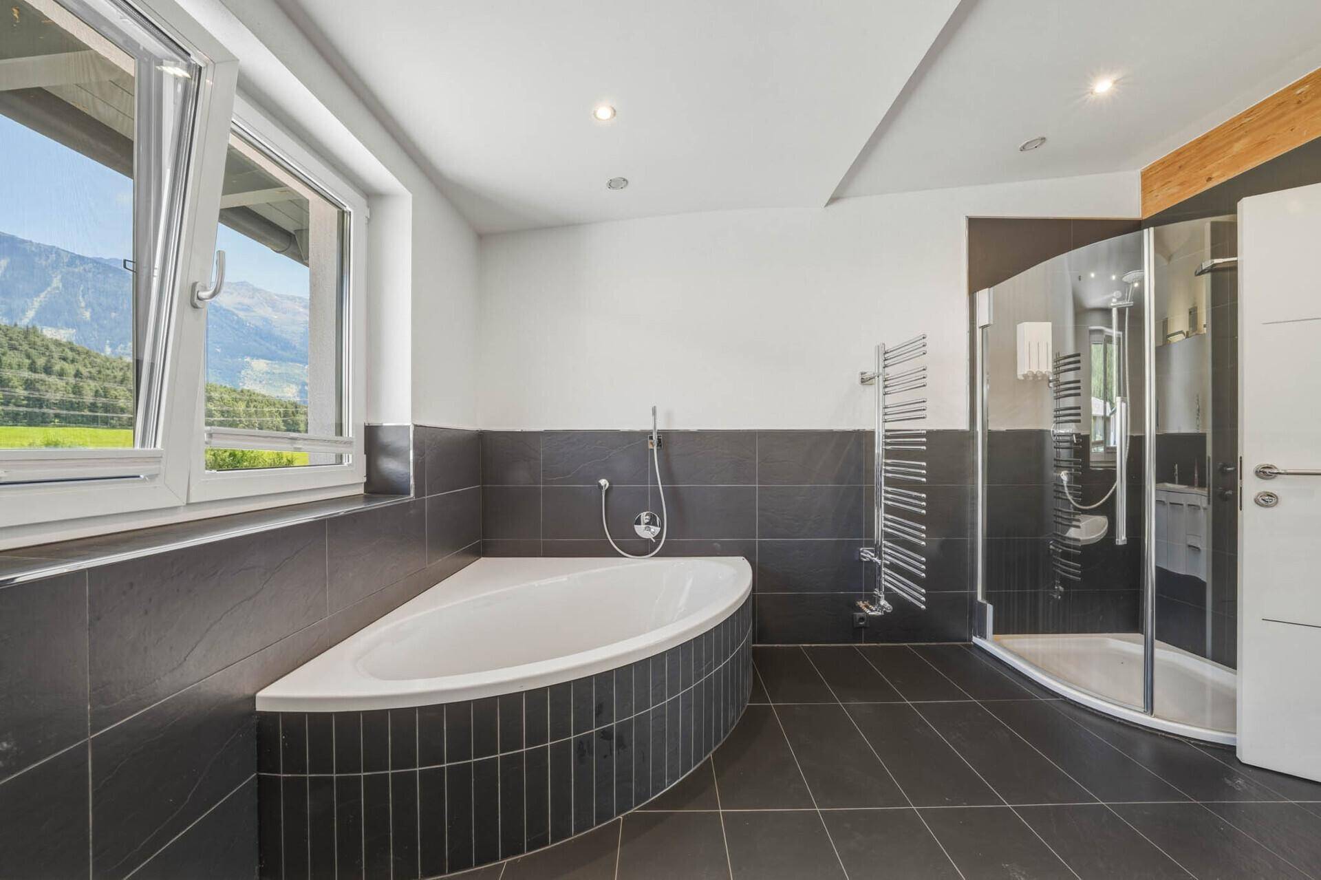Modernes Badezimmer mit Eckbadewanne, Duschkabine und Fenster mit Bergblick.