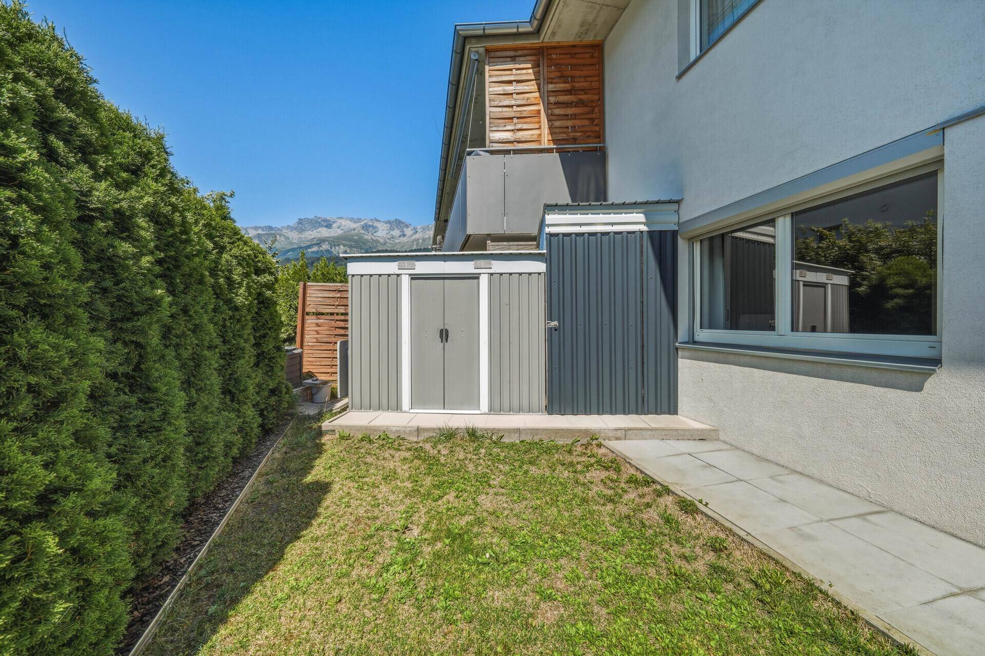Gepflegter Gartenbereich mit hoher Hecke, Rasenfläche und praktischen Gartenhäusern.
