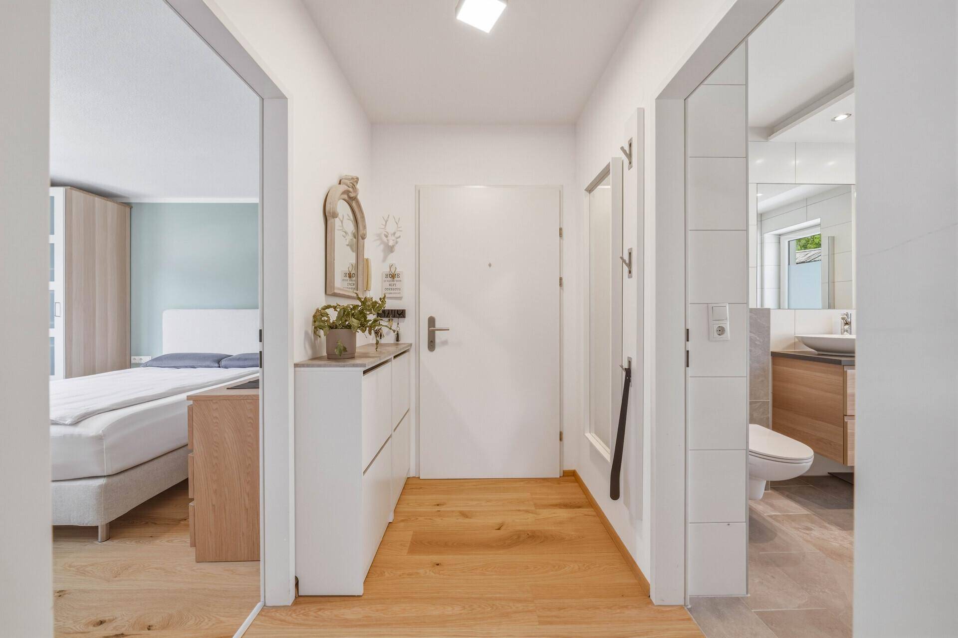 Heller Eingangsbereich mit Holzboden, Schuhschrank und Zugang zu Schlafzimmer und Bad.