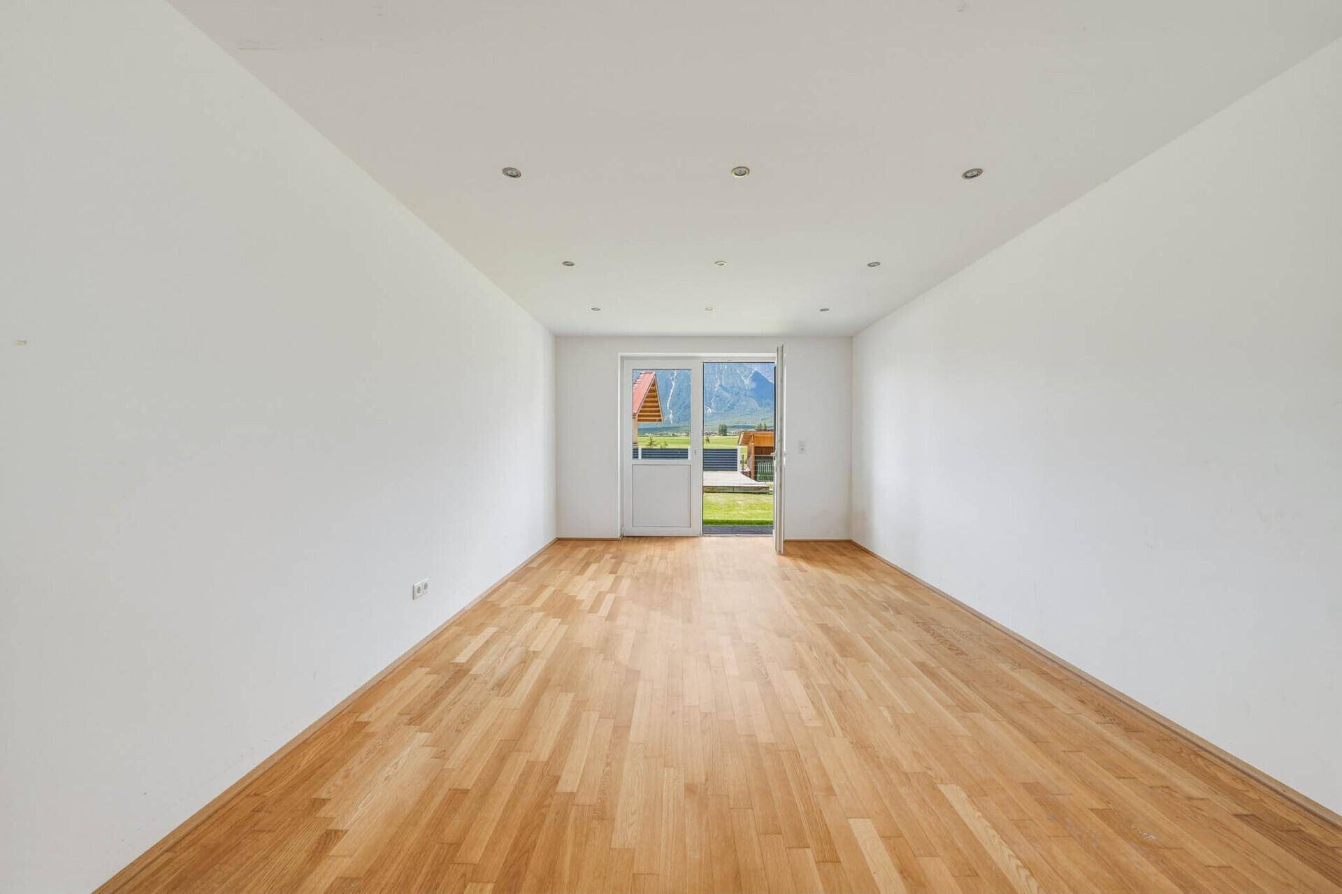 Helles Zimmer mit elegantem Holzboden und Zugang zu einem Außenbereich, ideal als Schlaf- oder Arbeitszimmer.