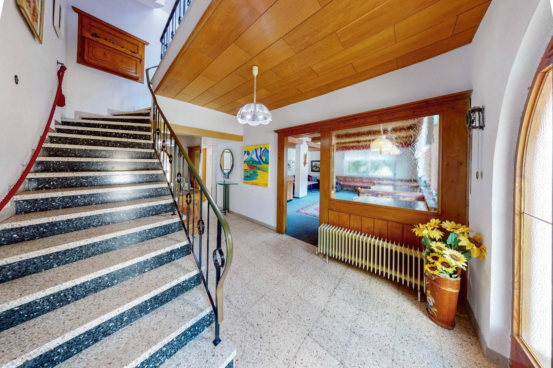 Heller Flur mit Treppe, Terrazzoboden und traditionellen Dekorationen.