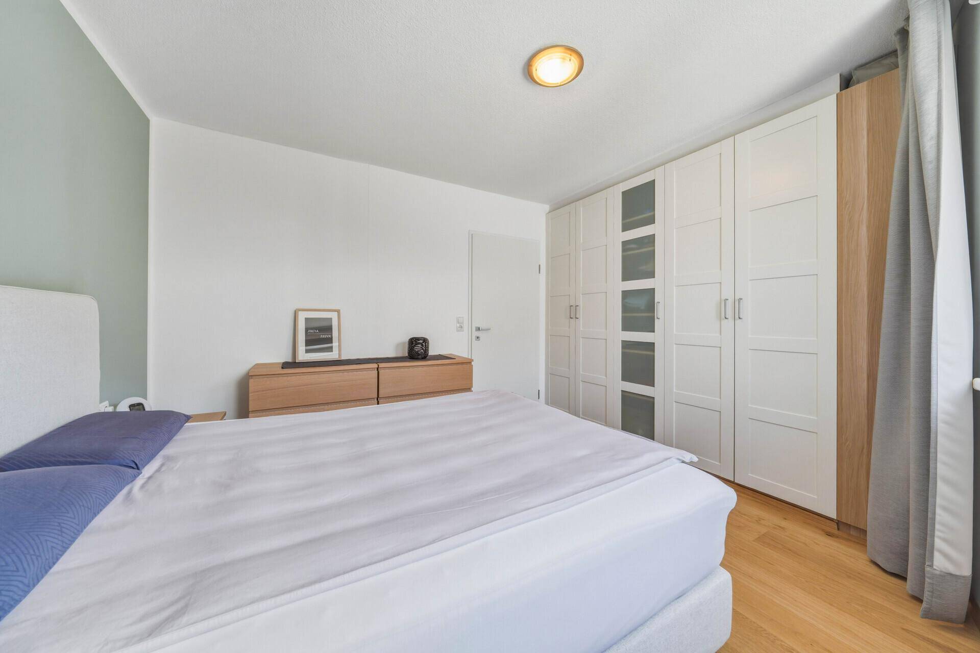 Schlafzimmer mit geräumigem Kleiderschrank, Holzboden und viel Tageslicht.