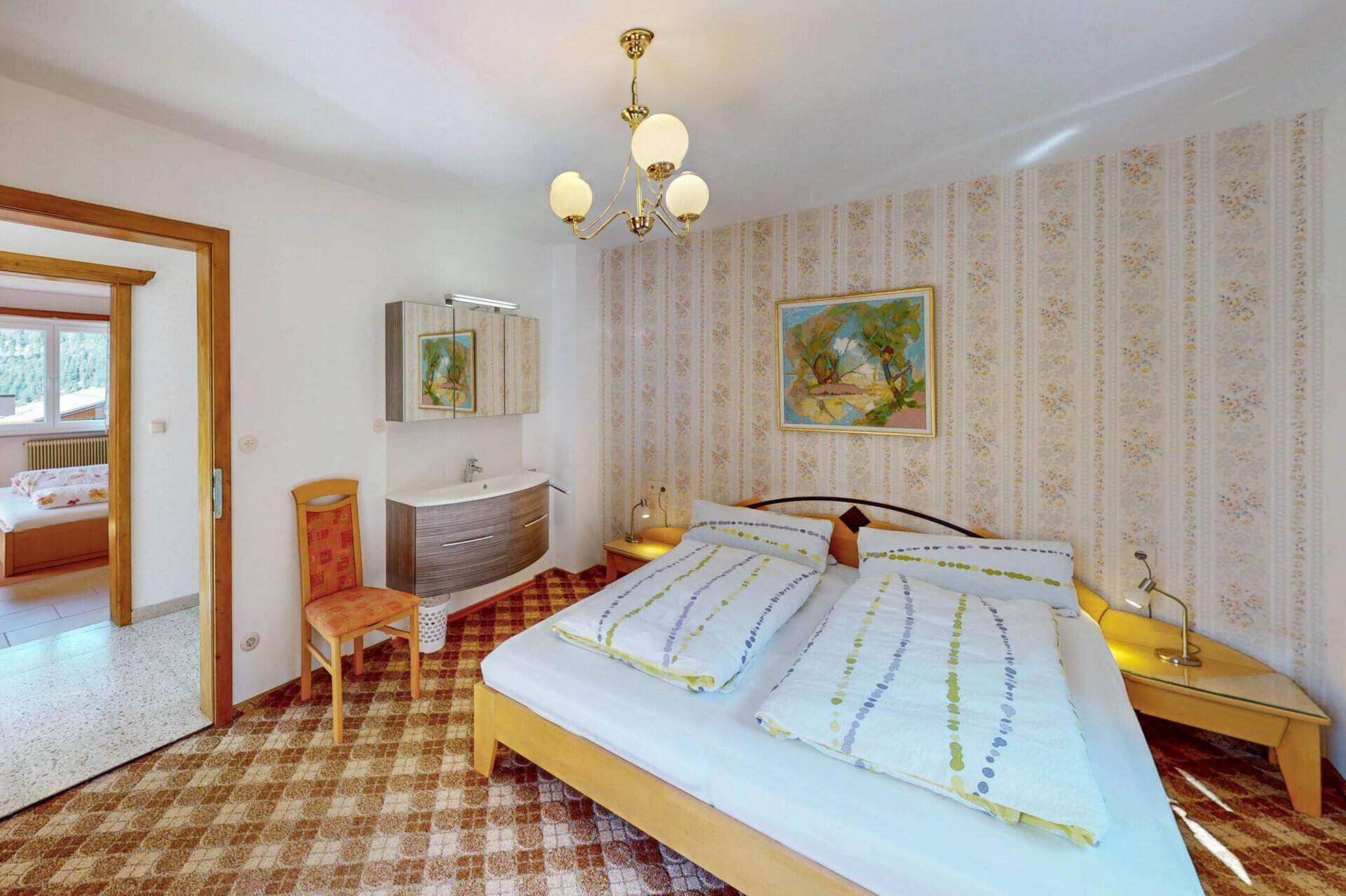 Gemütliches Schlafzimmer mit Doppelbett, Teppichboden und floraler Tapete.