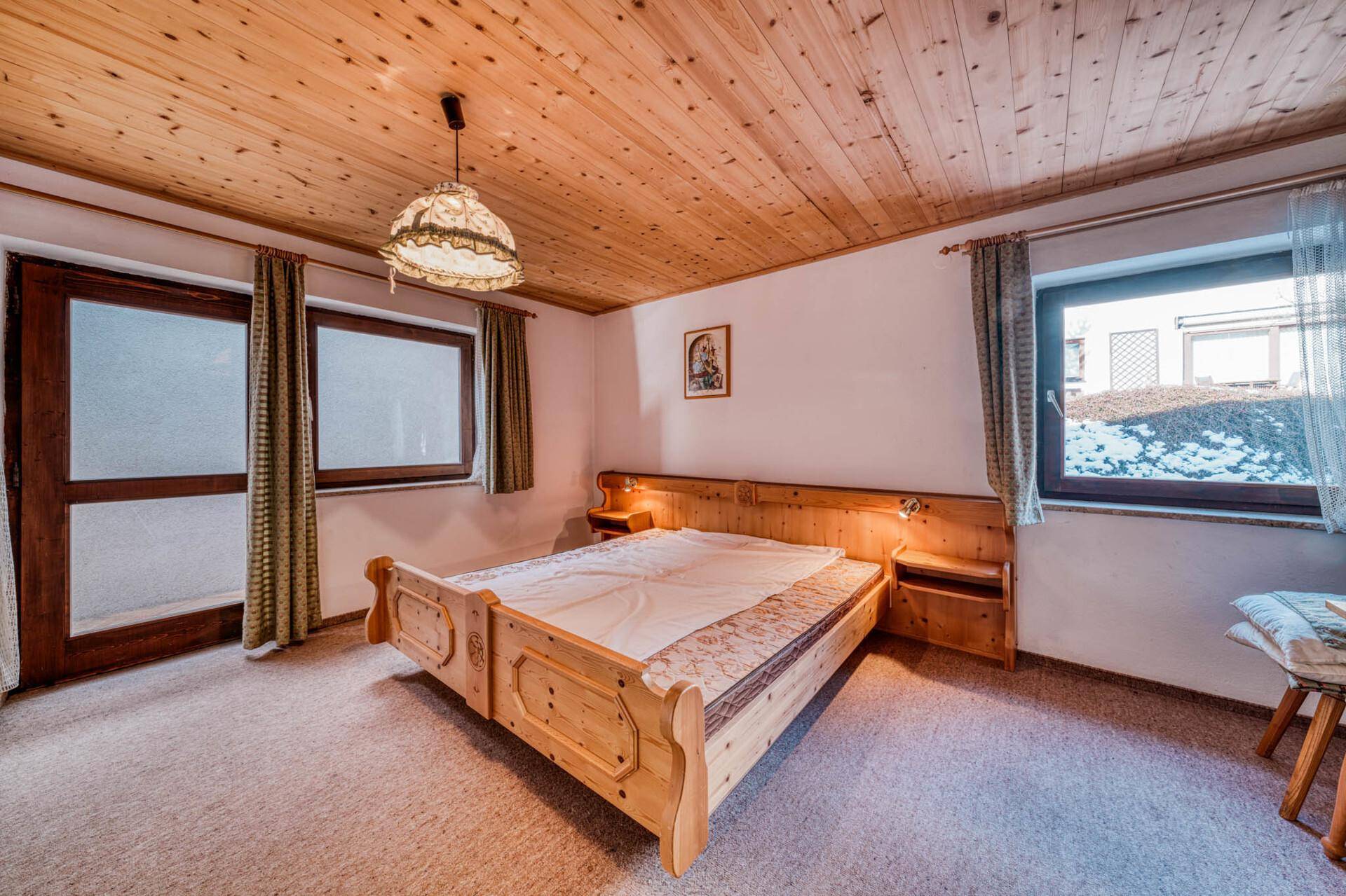 Schlafzimmer im Landhausstil mit Holzdecke, Teppichboden und Blick nach draußen.