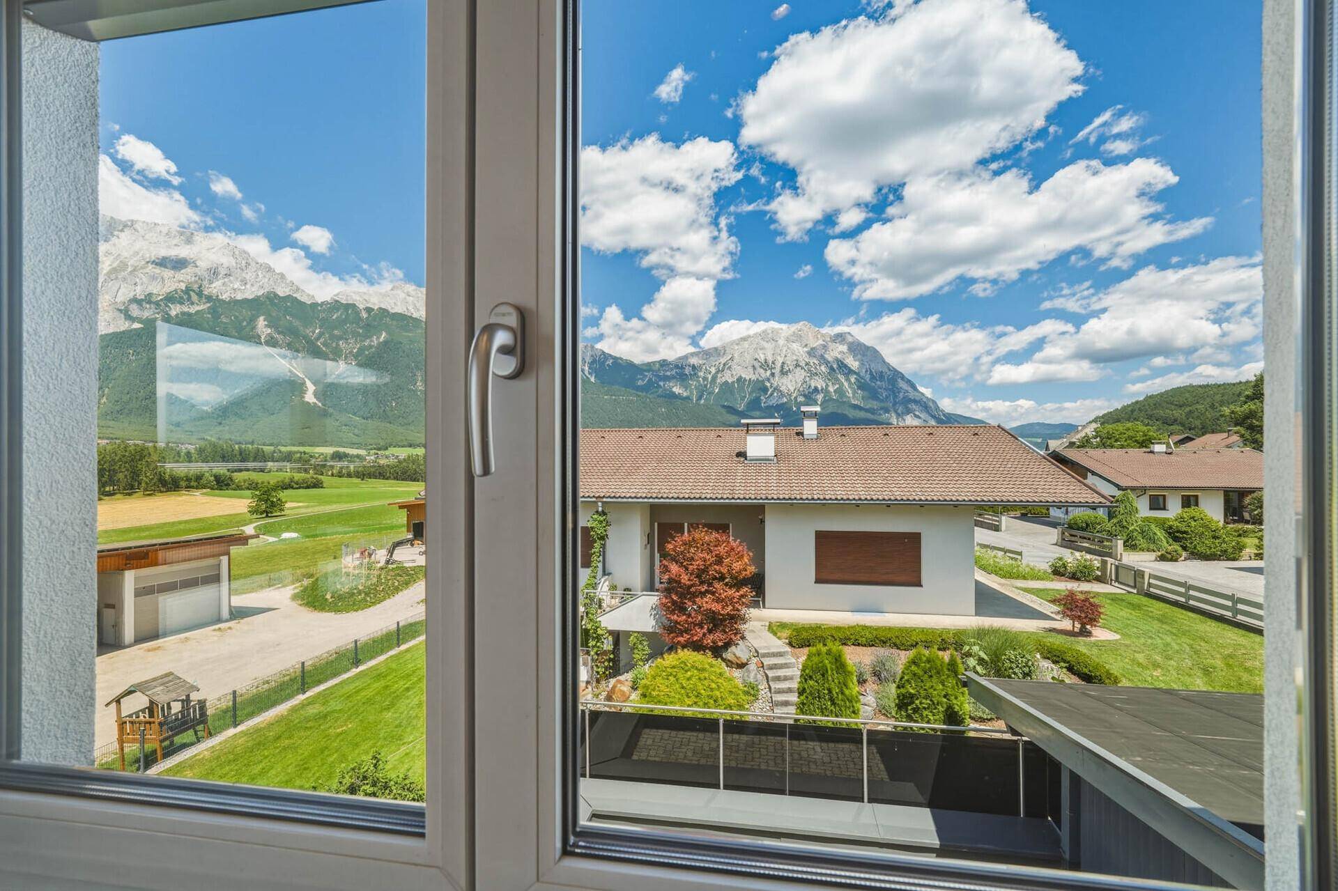 Malerischer Ausblick auf die umliegende Berglandschaft und benachbarte Häuser durch ein Fenster.