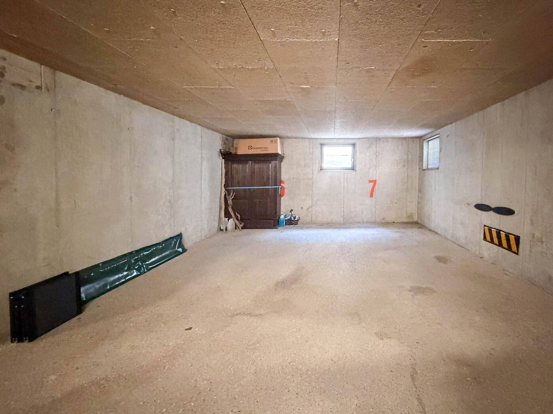Einfacher Kellerraum mit Betonwänden, kleinem Fenster und Stauraum für diverse Gegenstände.