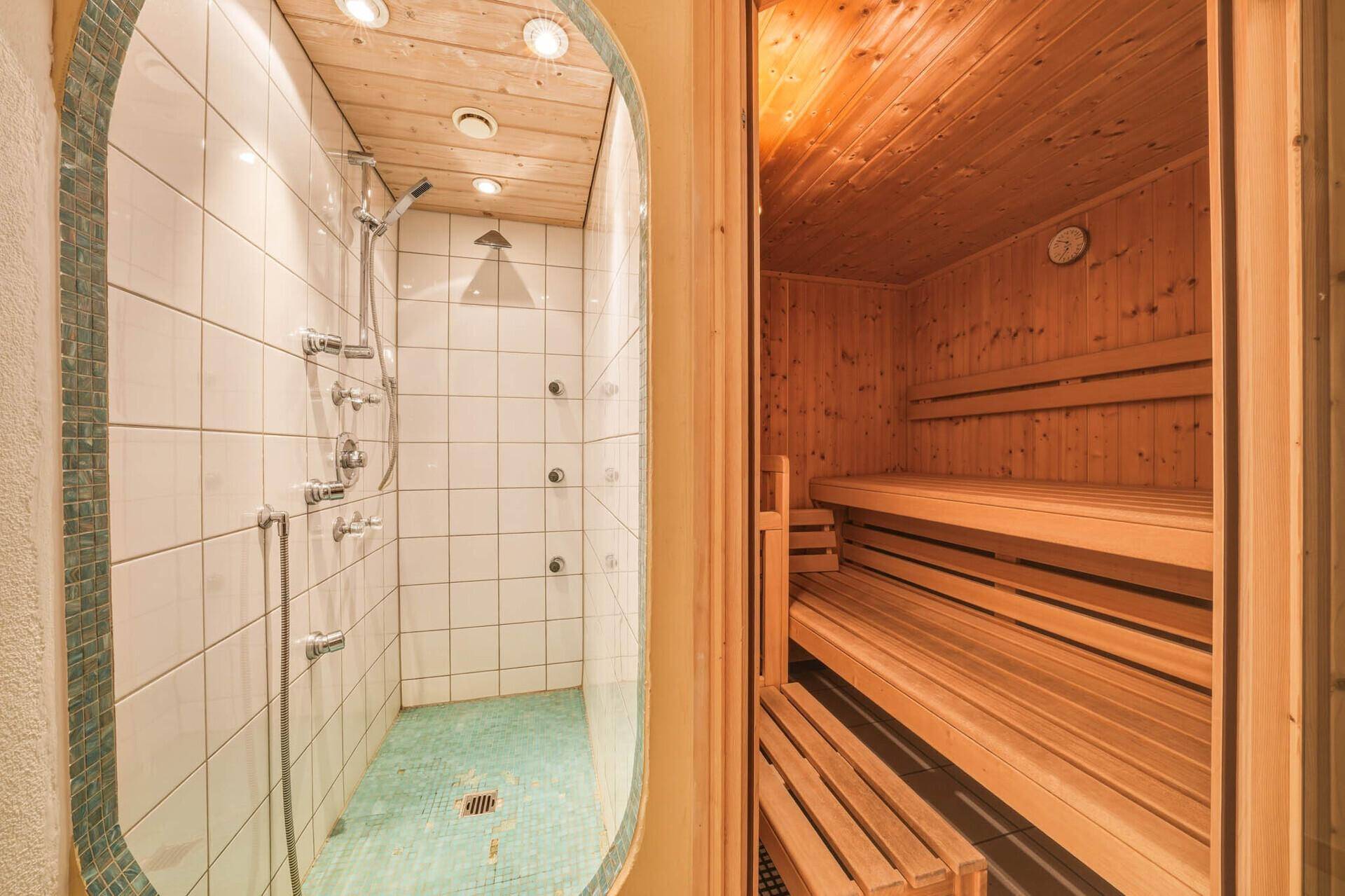 Modernes Badezimmer mit Duschbereich und angrenzender Holzsauna für Entspannung und Wellness.