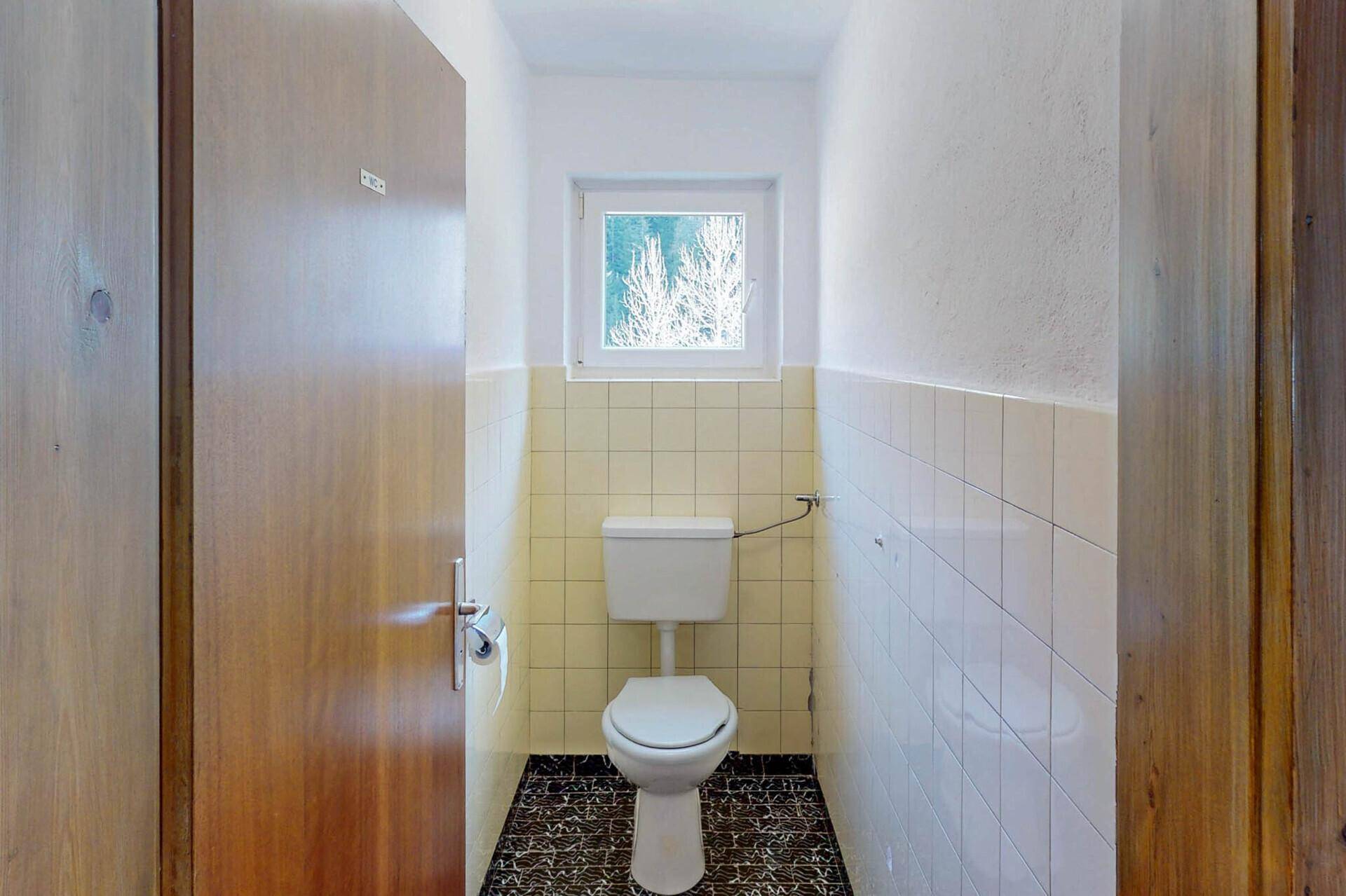 Kleines Badezimmer mit WC, Fenster und gelben Fliesen.