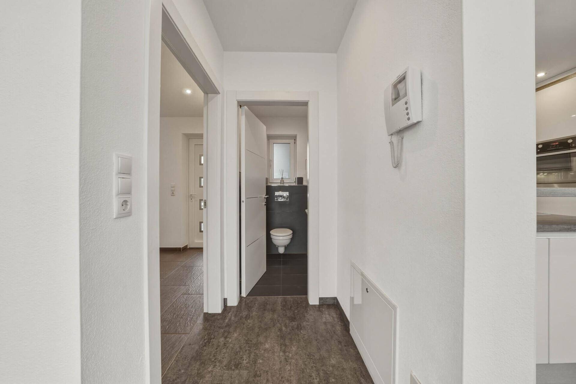 Heller Flur mit dunklem Fliesenboden, der zu einem Gäste-WC und weiteren Räumen führt.
