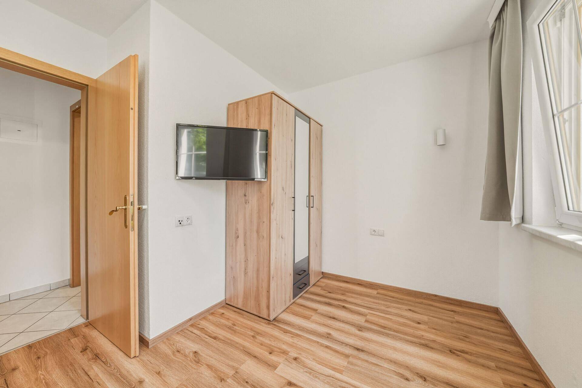 Schlafzimmerecke mit modernem Holzschrank, Wandfernseher und Holzboden.
