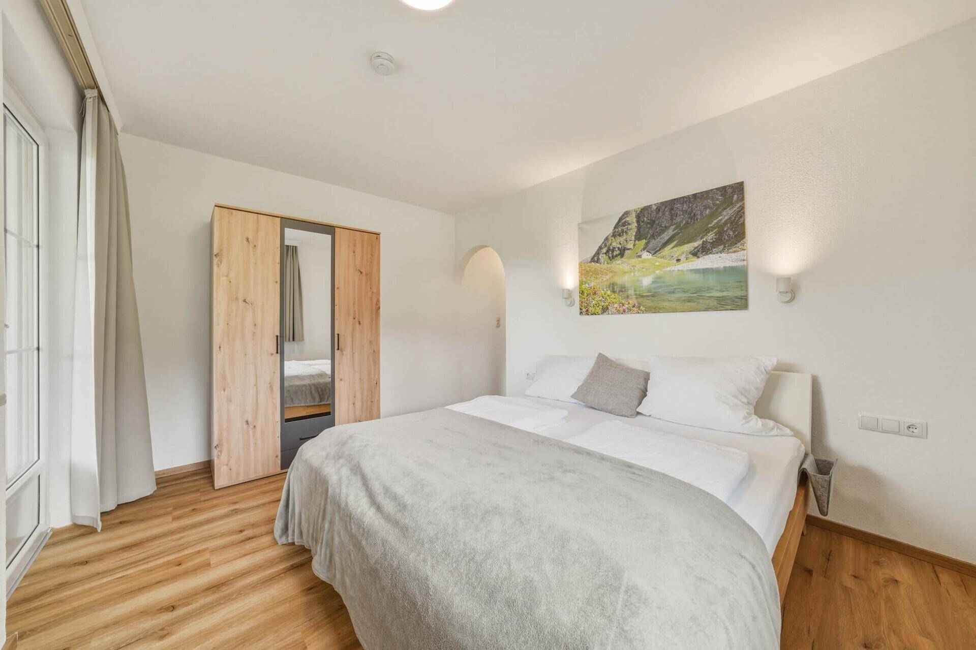 Helles Schlafzimmer mit Balkonzugang, Holzboden und modernem Kleiderschrank.