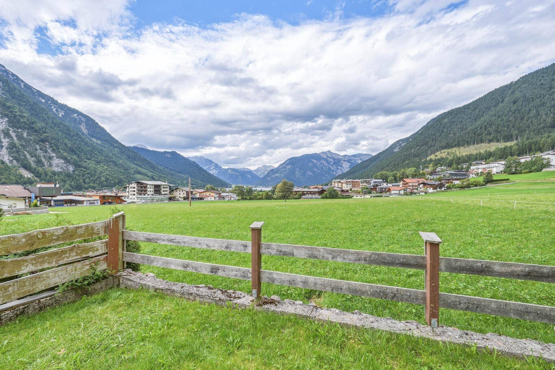 Malerischer Ausblick über grüne Felder auf einen See und die umliegende Berglandschaft.