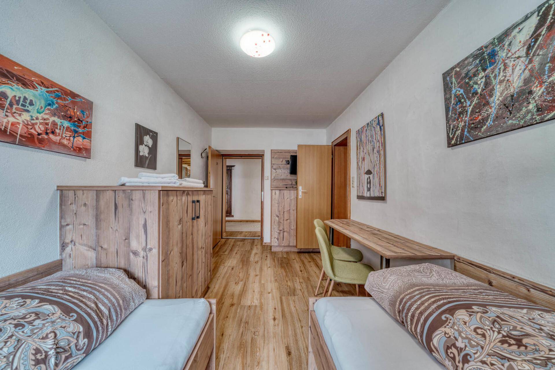 Schlafzimmer mit zwei Einzelbetten, Holzboden und moderner Kunst, funktional und hell.