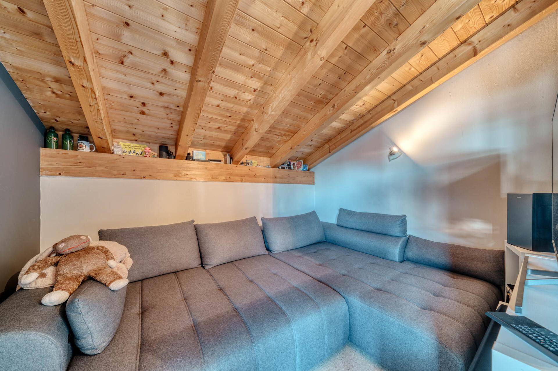 Gemütlicher Wohnbereich im Dachgeschoss mit großer Couch und Holzbalkendecke.