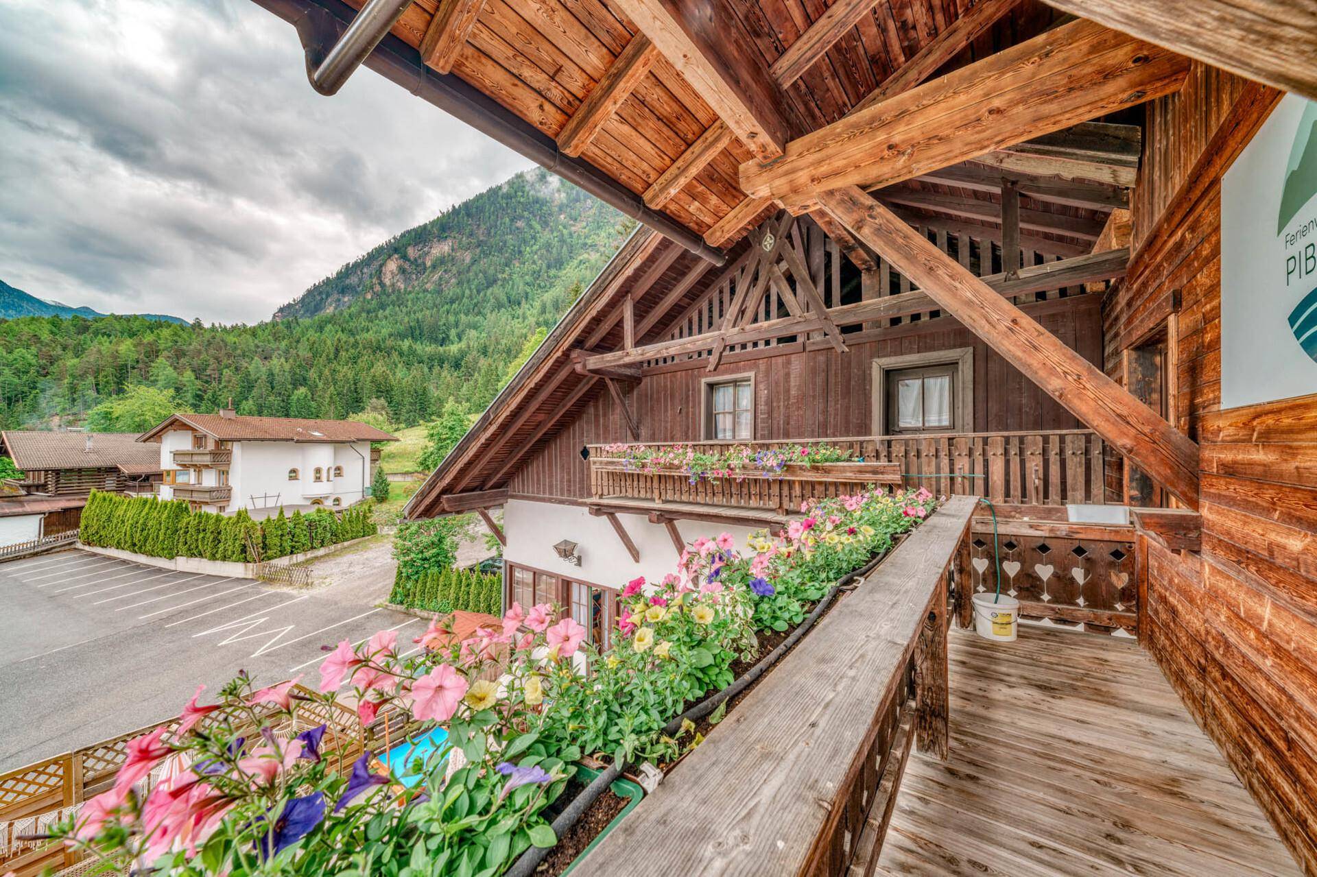 Traditioneller Holzbalkon mit bunten Blumenkästen und Blick auf die Umgebung.