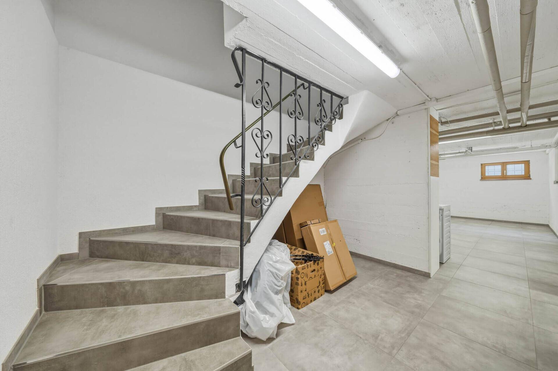 Treppenabgang in einen Kellerraum mit grauen Fliesen und Stauraum unter der Treppe.
