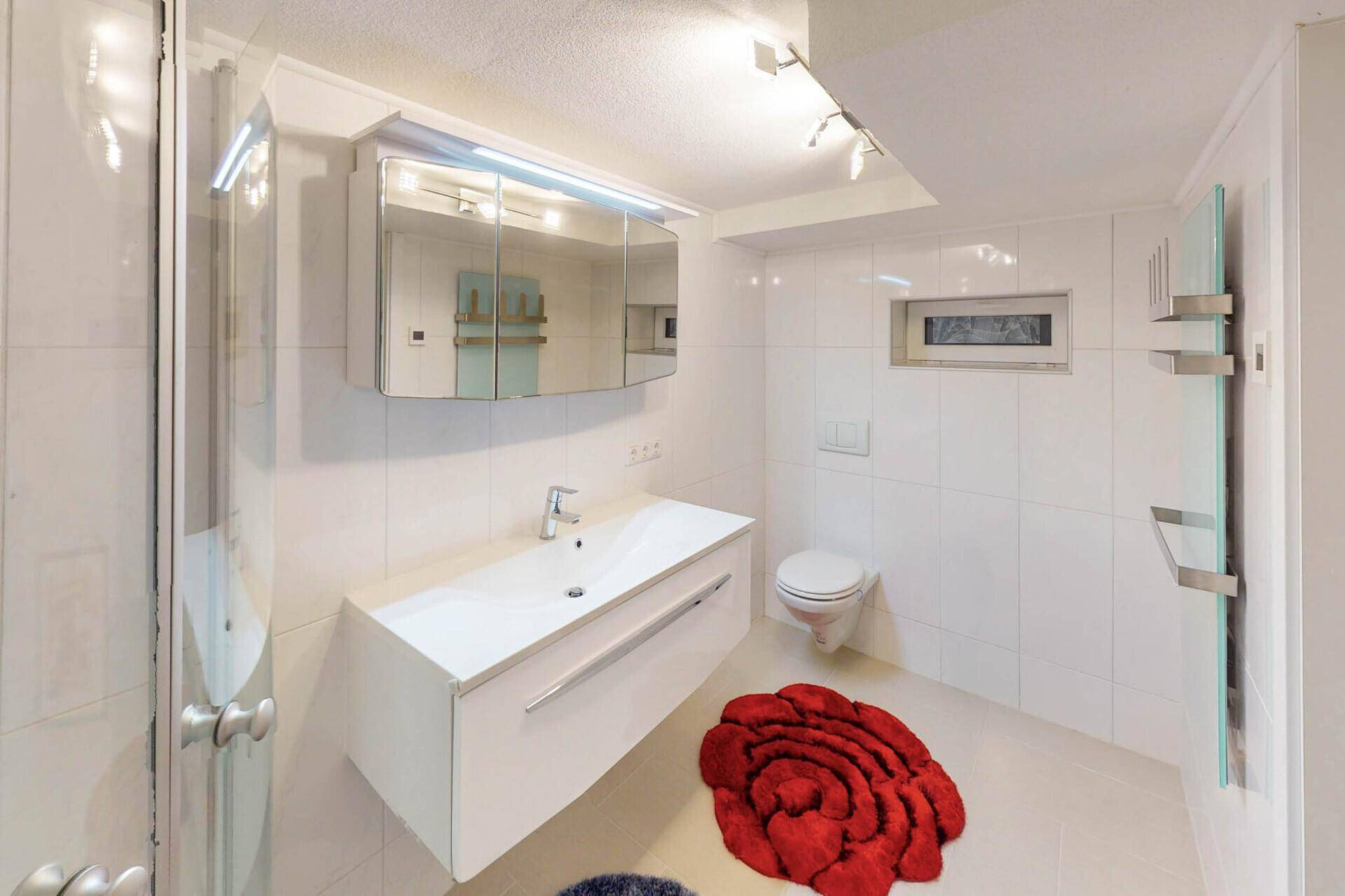 Modernes Badezimmer mit Duschkabine, WC, Waschbecken und Spiegelschrank.