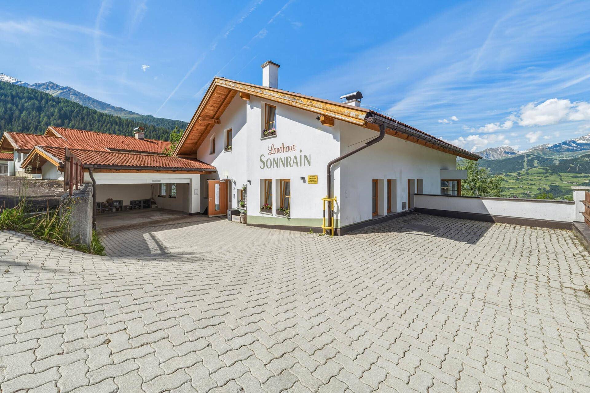 Traditionelles Haus mit großem gepflastertem Vorplatz und Bergblick, umgeben von Natur.