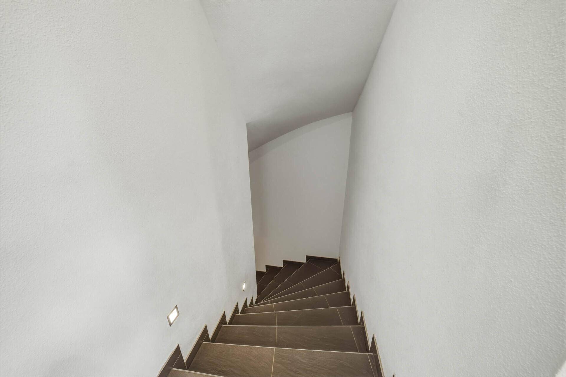 Modernes Treppenhaus mit dunklen Fliesenstufen und integrierter Wandbeleuchtung.