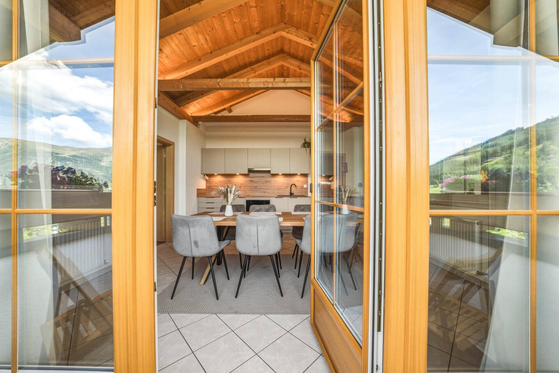 Blick durch die Balkontür in den hellen Wohn-Essbereich mit moderner Küche und Bergblick.