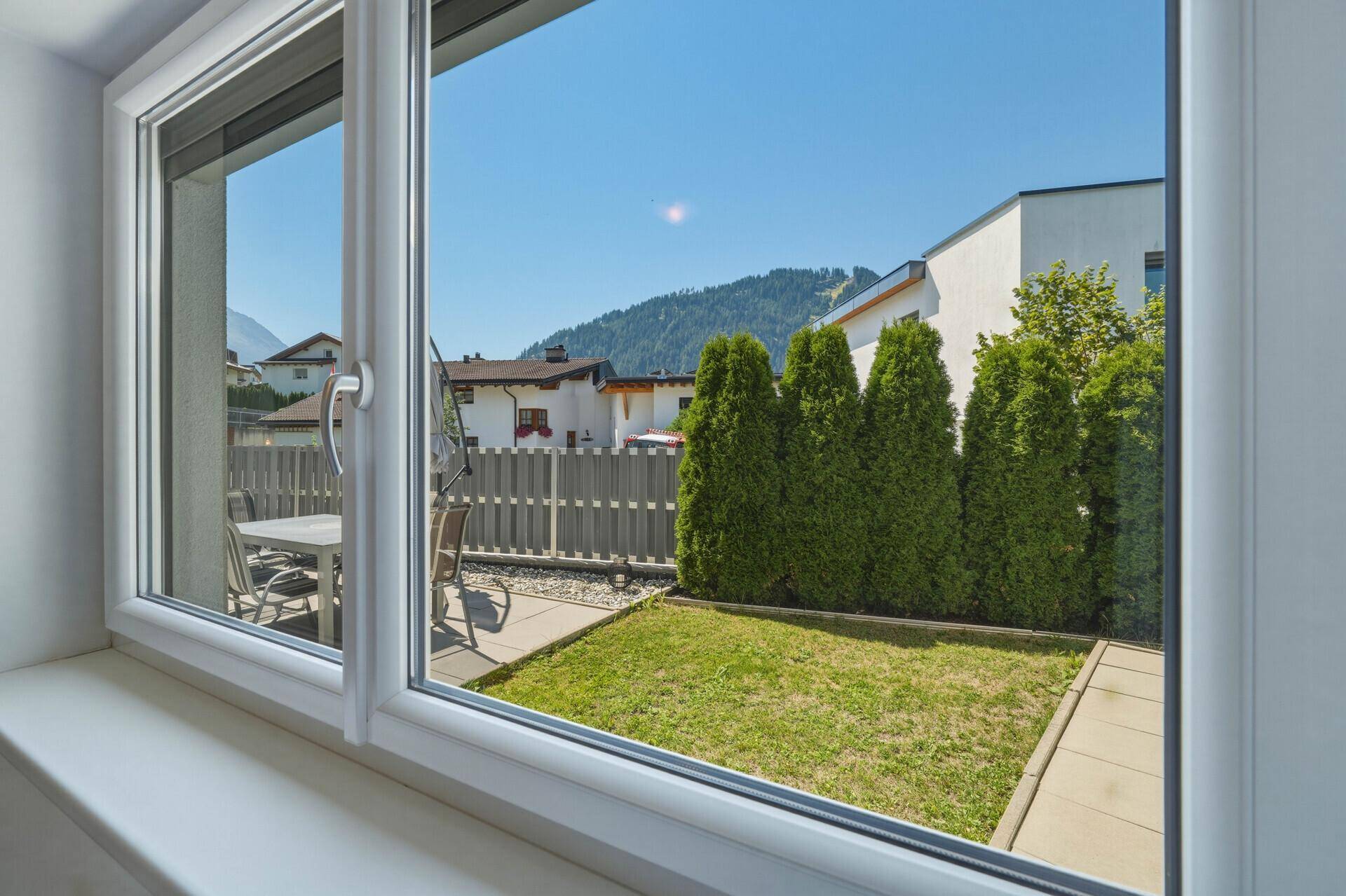 Blick aus dem Fenster auf den kleinen Gartenbereich mit Rasen und Bergblick.
