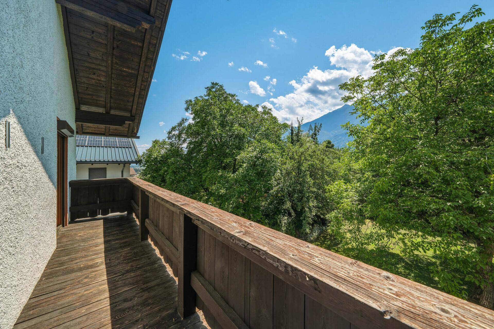 Langer Holzbalkon mit Blick auf grüne Bäume und die umliegenden Berge.